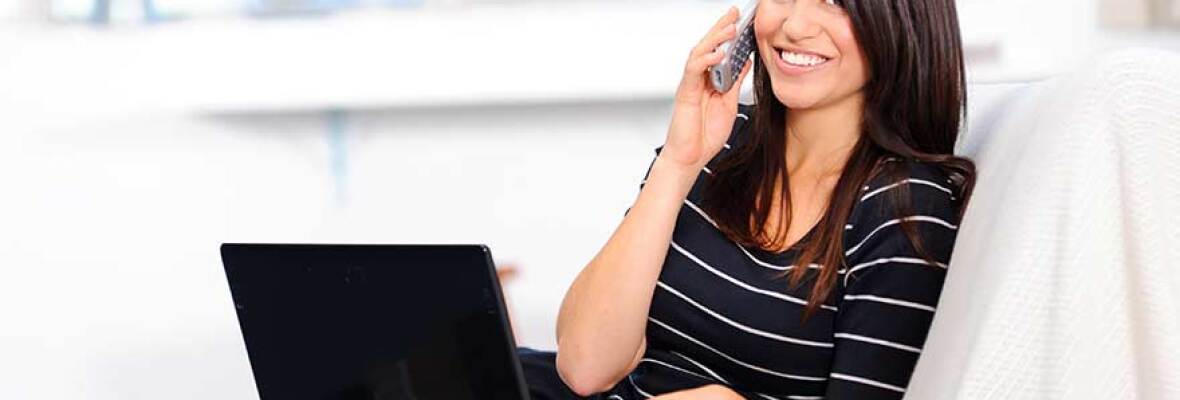 Woman in striped shirt talking on the phone and using a black laptop